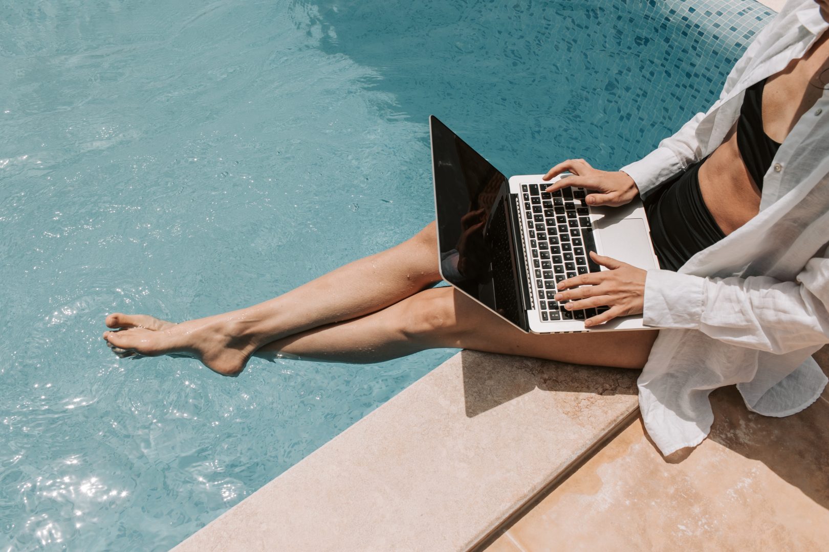 woman sitting on the edge of a pool with a laptop at The Legacy at Veramendi